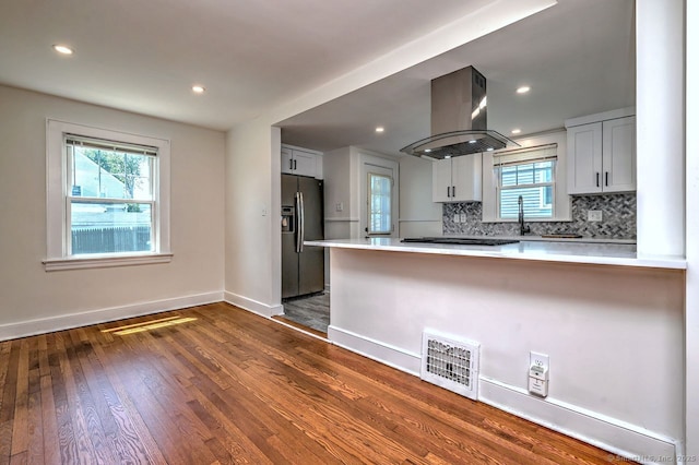kitchen featuring island exhaust hood, fridge with ice dispenser, a peninsula, plenty of natural light, and recessed lighting