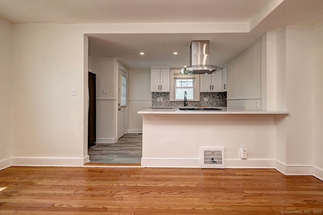 kitchen with exhaust hood, light countertops, a peninsula, backsplash, and recessed lighting