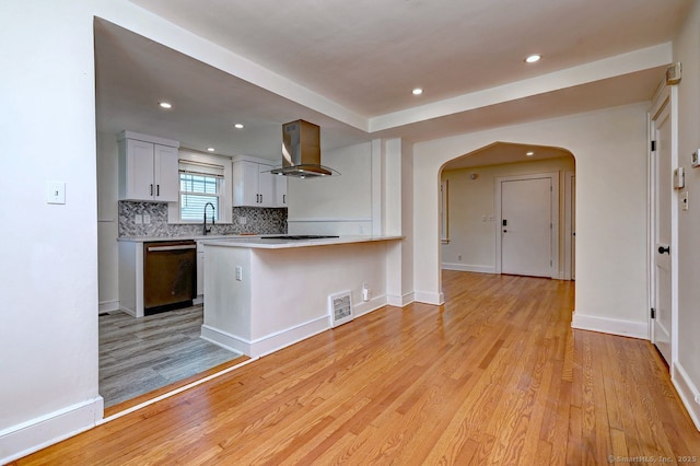 kitchen with black dishwasher, range hood, arched walkways, tasteful backsplash, and light wood finished floors