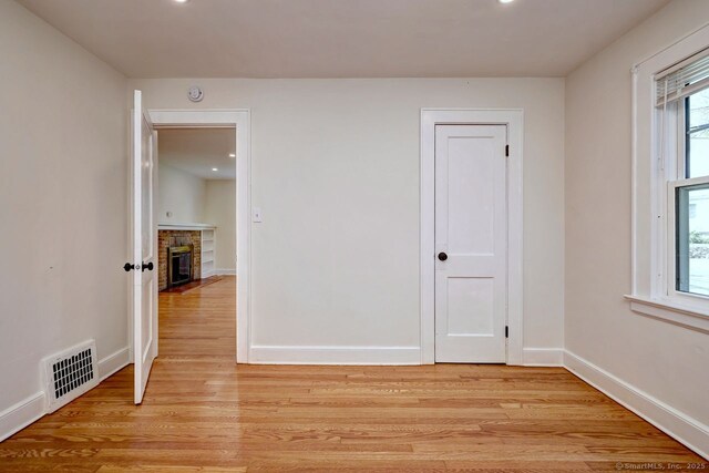 empty room featuring a fireplace with flush hearth, light wood-type flooring, baseboards, recessed lighting, and a smoke detector