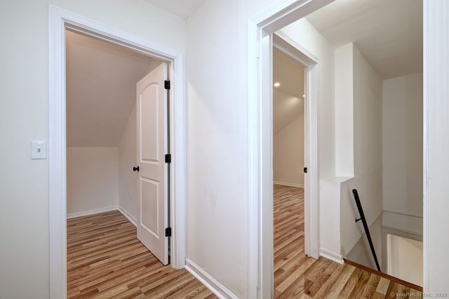 corridor featuring light wood-style flooring, an upstairs landing, vaulted ceiling, and baseboards
