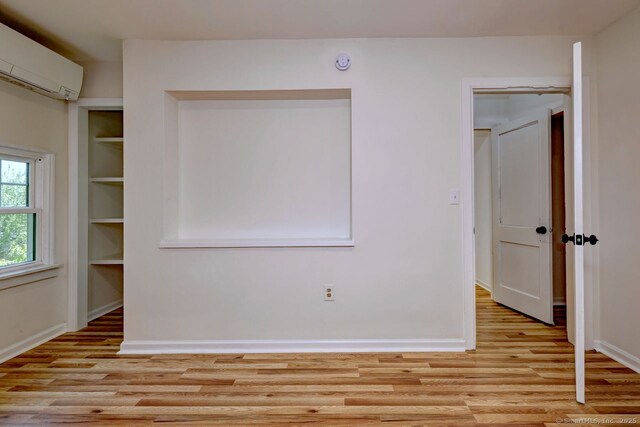 unfurnished room with a wall unit AC, light wood-style flooring, baseboards, and a smoke detector