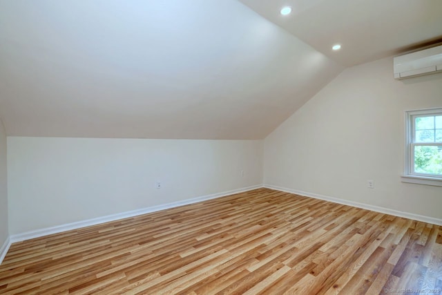 bonus room with a wall unit AC, lofted ceiling, light wood-style flooring, baseboards, and recessed lighting