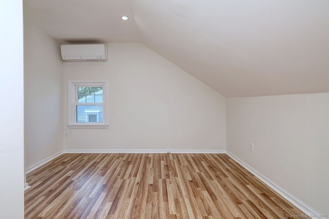 additional living space with a wall unit AC, light wood-style flooring, lofted ceiling, baseboards, and recessed lighting