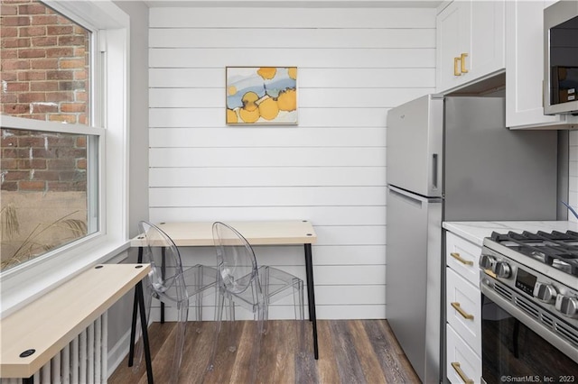 kitchen with appliances with stainless steel finishes, white cabinetry, light countertops, dark wood finished floors, and wooden walls