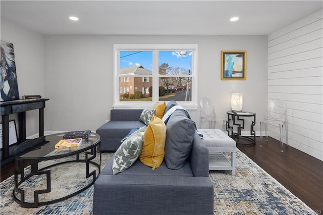 living room featuring dark wood-type flooring, baseboards, recessed lighting, and wood walls