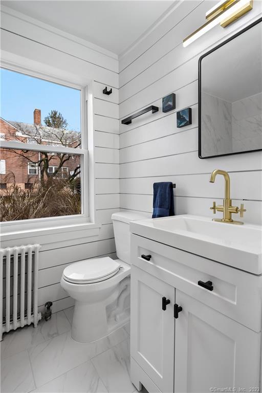 bathroom featuring radiator heating unit, marble look tiles, toilet, vanity, and wood walls