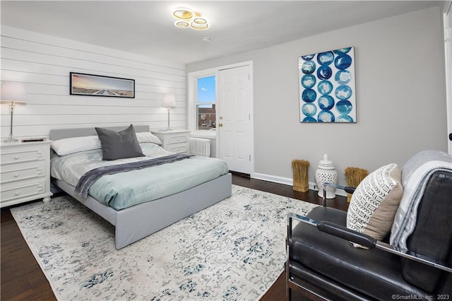 bedroom with radiator heating unit, wood finished floors, baseboards, and wood walls