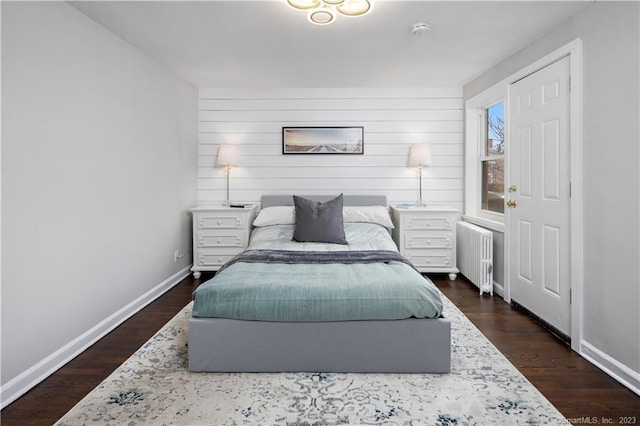 bedroom with radiator heating unit, baseboards, dark wood-style flooring, and wood walls