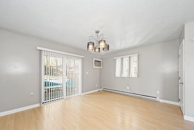 spare room with a baseboard heating unit, wood finished floors, a chandelier, and plenty of natural light