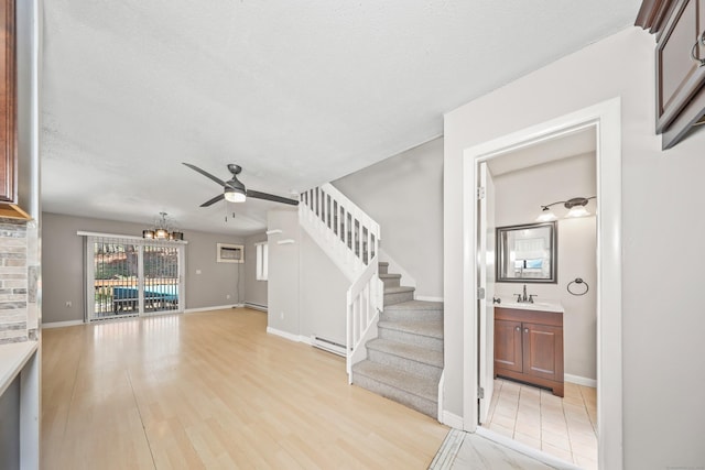 unfurnished living room featuring a ceiling fan, a baseboard heating unit, a baseboard radiator, stairs, and a chandelier
