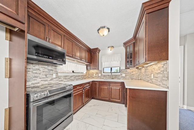 kitchen featuring stainless steel appliances, light marble finish floors, light countertops, a sink, and glass insert cabinets