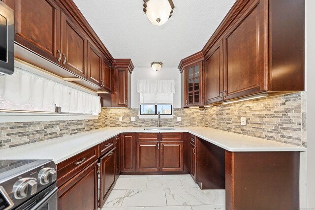 kitchen with a sink, stainless steel range with electric cooktop, light marble finish floors, light countertops, and glass insert cabinets