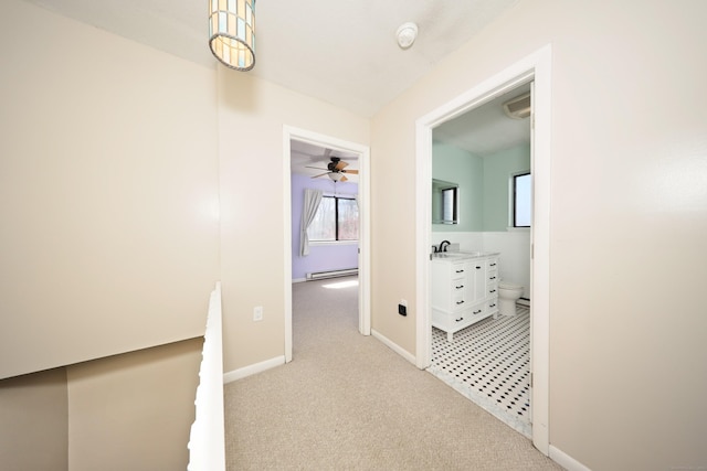 hall featuring light colored carpet, a sink, baseboards, and a baseboard heating unit