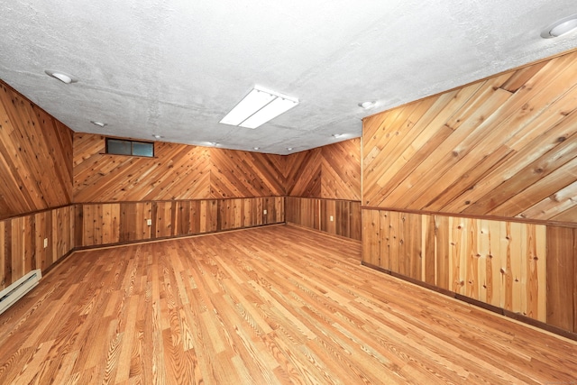 bonus room with wood walls, wood finished floors, and a baseboard radiator