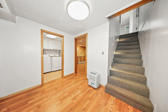 stairs with washing machine and clothes dryer, wood finished floors, a textured ceiling, and baseboards
