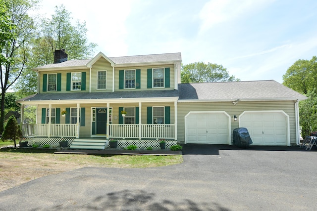 colonial inspired home with an attached garage, covered porch, a chimney, and asphalt driveway