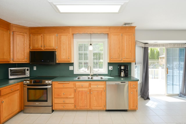 kitchen with appliances with stainless steel finishes, a sink, dark countertops, and light tile patterned floors