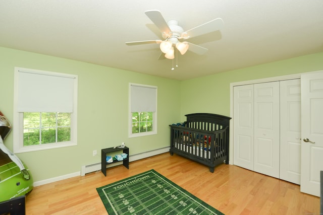 bedroom with wood finished floors, a closet, baseboards, a baseboard heating unit, and ceiling fan
