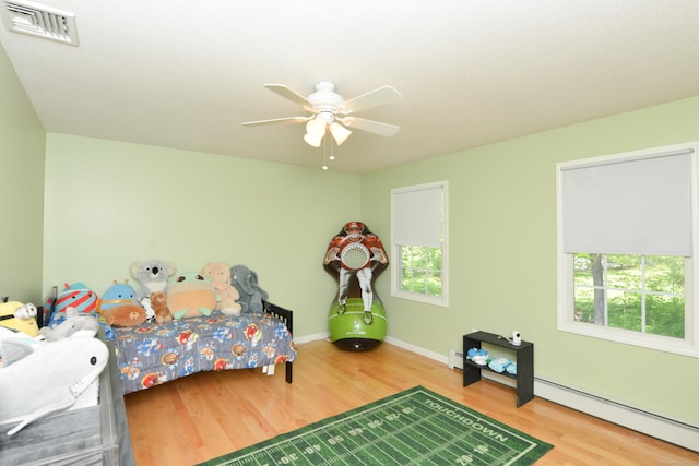 bedroom featuring wood finished floors, baseboard heating, ceiling fan, and baseboards
