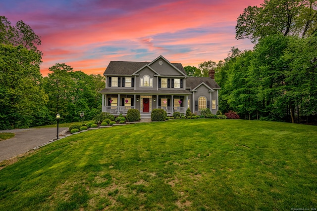 colonial home featuring a porch, a chimney, and a yard