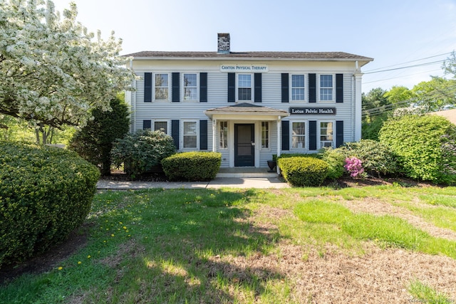 colonial-style house featuring a chimney and a front yard