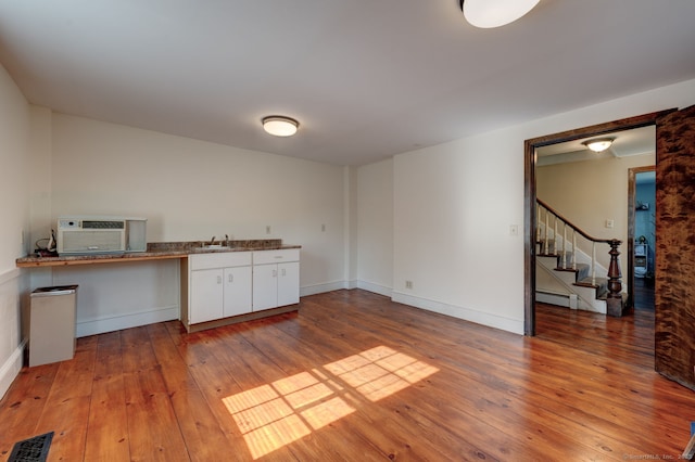 spare room with wood-type flooring, stairway, a baseboard radiator, baseboards, and a sink