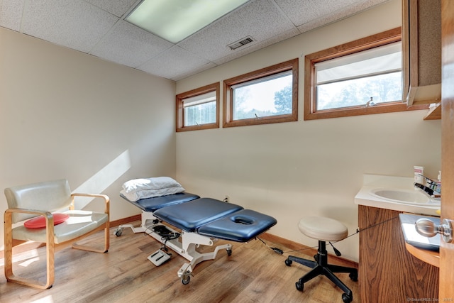 exercise area featuring wood finished floors, a paneled ceiling, and baseboards