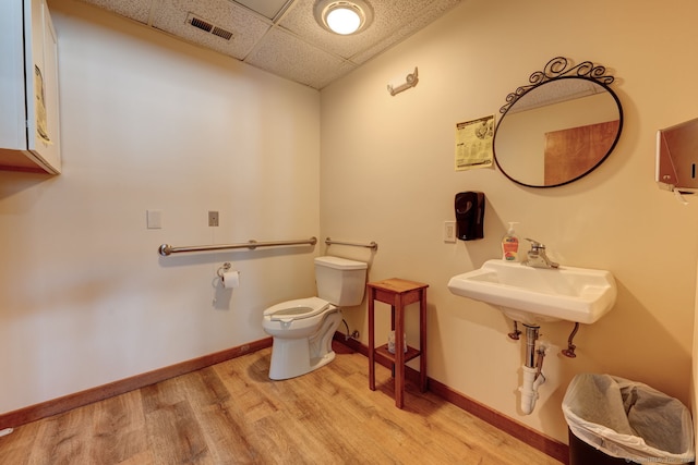 bathroom with a drop ceiling, wood finished floors, toilet, baseboards, and a sink