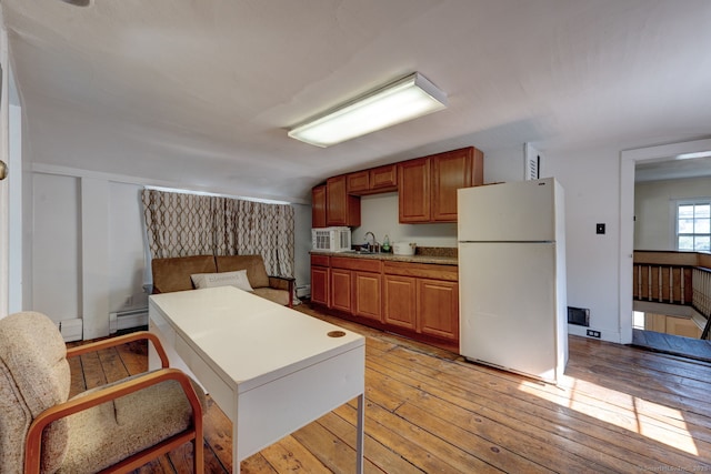 kitchen with freestanding refrigerator, a sink, light wood-type flooring, and baseboard heating