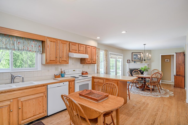 kitchen with white appliances, a sink, under cabinet range hood, light countertops, and decorative backsplash
