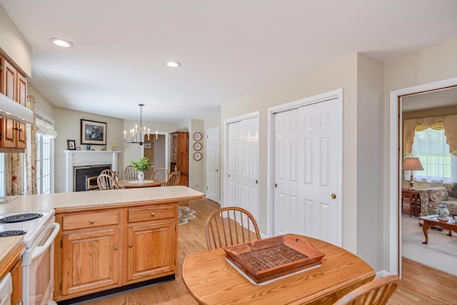 kitchen with light wood finished floors, a fireplace, a peninsula, white electric range, and light countertops