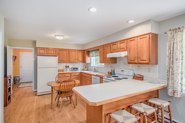 kitchen featuring white appliances, under cabinet range hood, a sink, a peninsula, and light countertops