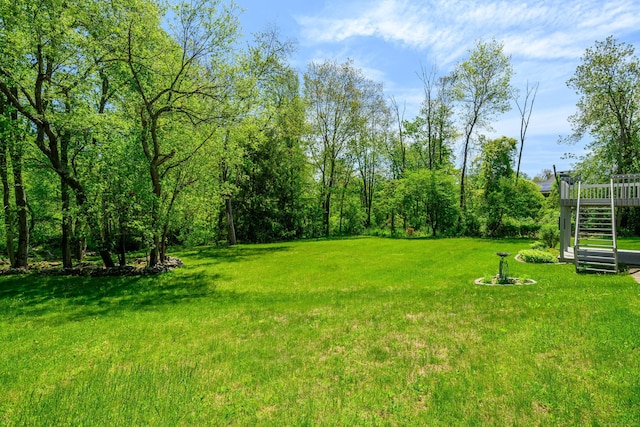 view of green lawn with a wooden deck and stairway