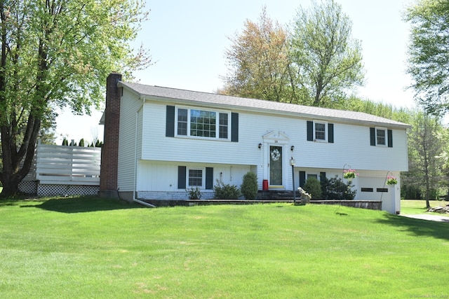 raised ranch with a chimney, an attached garage, and a front lawn