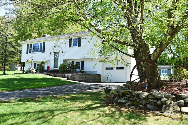 bi-level home with an attached garage, driveway, a front yard, and a chimney