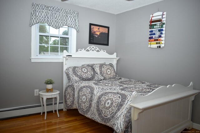 bedroom with a baseboard heating unit and wood finished floors