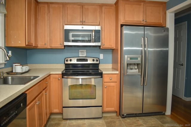 kitchen with stainless steel appliances, a sink, light countertops, and brown cabinetry