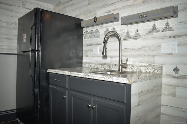 kitchen featuring a sink, freestanding refrigerator, and light stone countertops