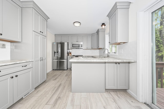 kitchen with appliances with stainless steel finishes, gray cabinets, tasteful backsplash, and a peninsula