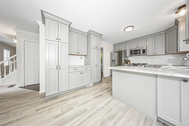 kitchen with stainless steel appliances, gray cabinetry, ornamental molding, a sink, and a peninsula