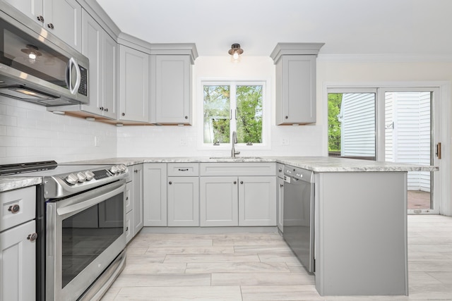 kitchen with appliances with stainless steel finishes, a sink, a peninsula, gray cabinetry, and crown molding