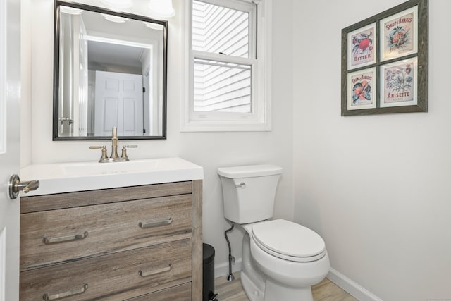 half bathroom with baseboards, vanity, toilet, and wood finished floors