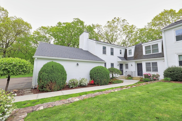view of front of home featuring a shingled roof, a front lawn, and a chimney