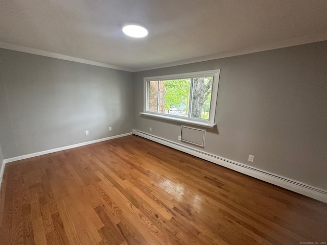 spare room featuring baseboard heating, ornamental molding, wood finished floors, and baseboards