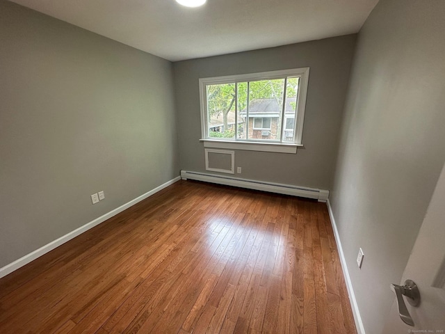unfurnished room with a baseboard heating unit, dark wood-type flooring, and baseboards