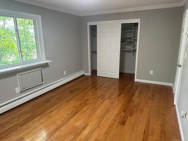 unfurnished bedroom featuring a baseboard heating unit, a closet, wood finished floors, baseboards, and crown molding