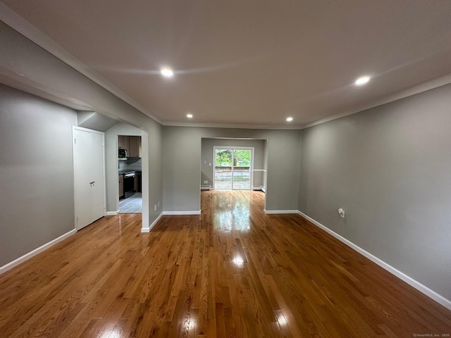 unfurnished living room with wood finished floors, baseboards, recessed lighting, and ornamental molding
