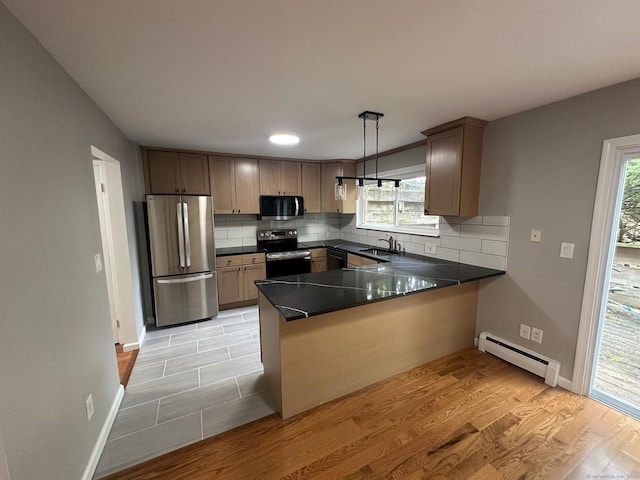 kitchen featuring appliances with stainless steel finishes, a baseboard heating unit, a sink, a peninsula, and dark countertops
