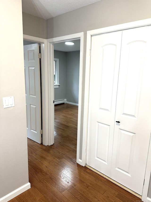 corridor featuring dark wood-type flooring, a baseboard radiator, and baseboards